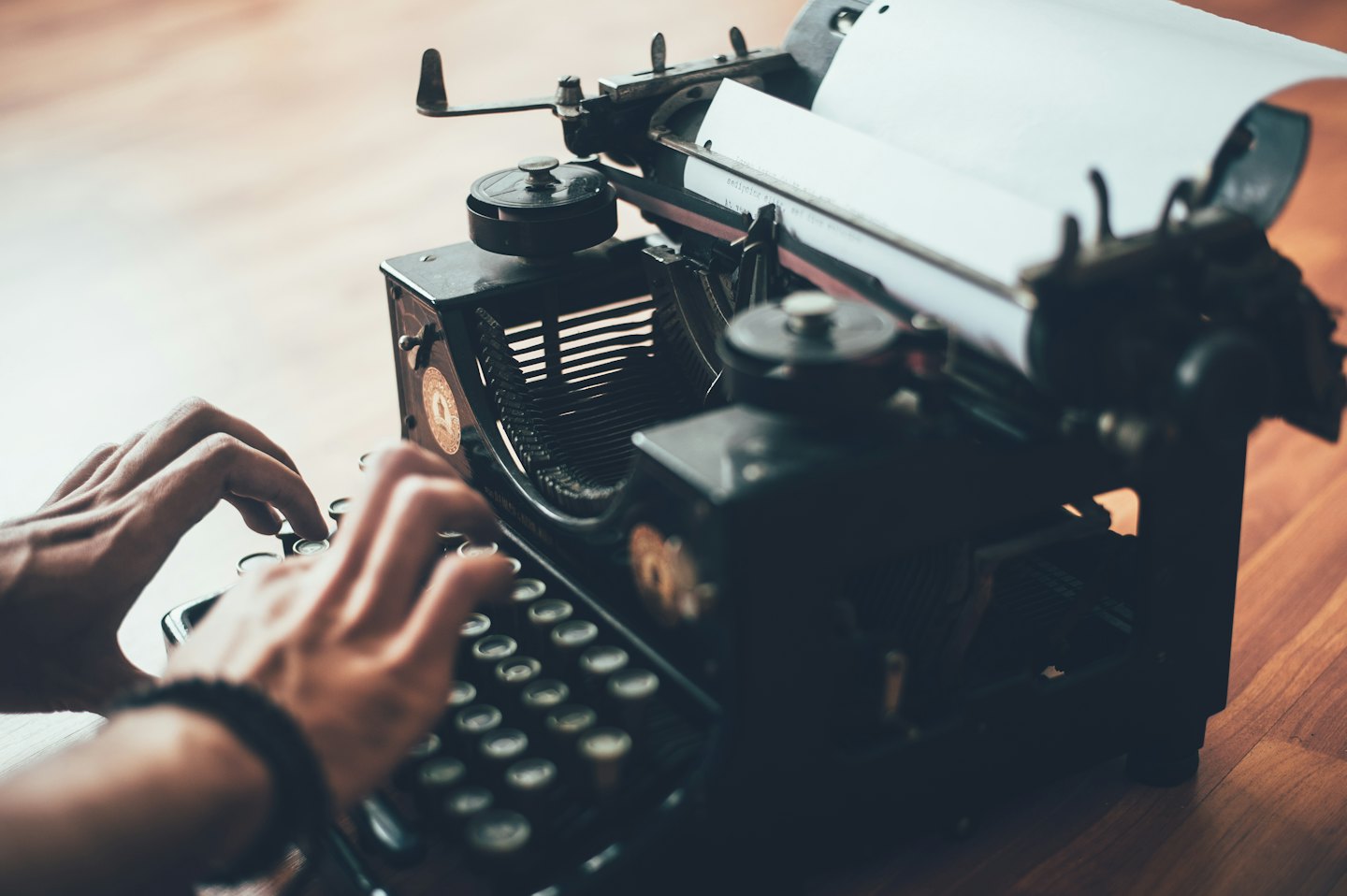 Hands typing on a vintage black typewriter on a wooden desk.